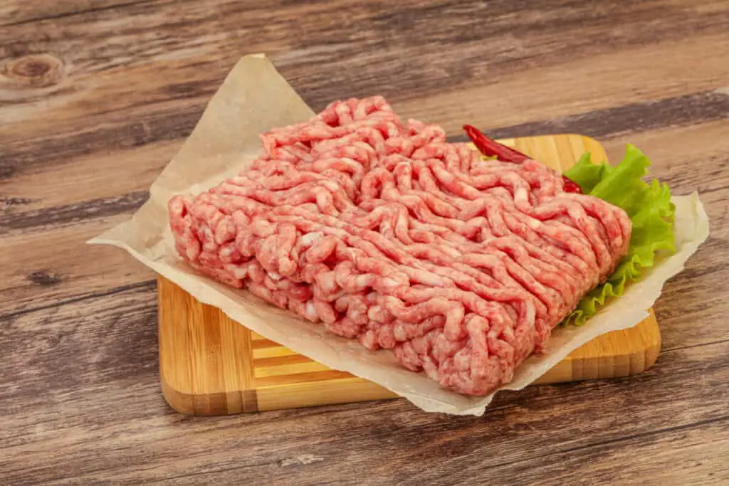 Raw ground beef on a wooden cutting board on a wooden table