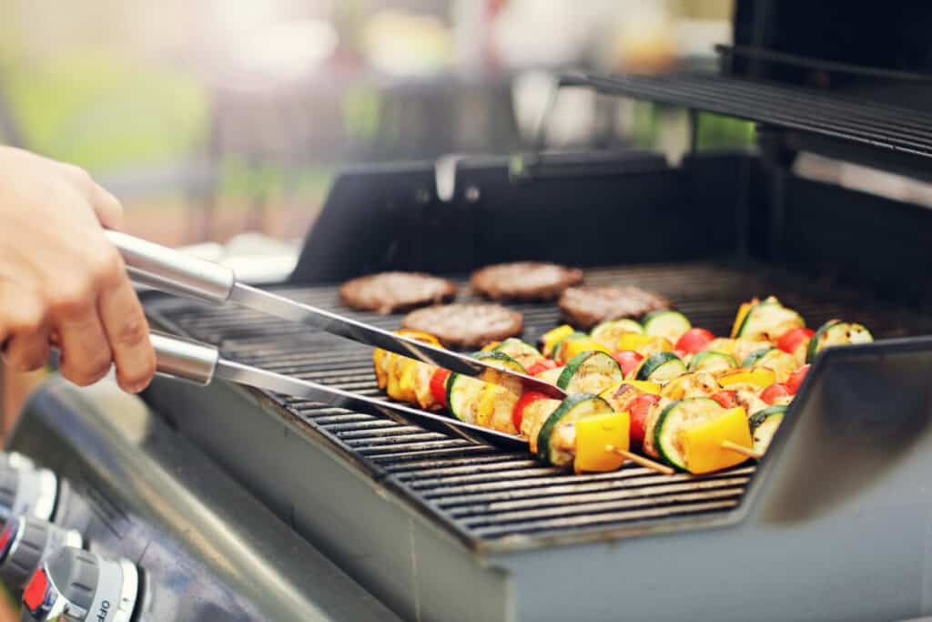 Vegetable skewers grilling next to hamburgers on a barbecue