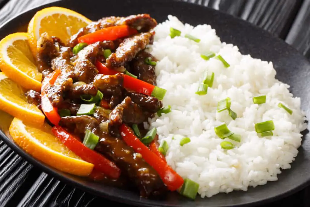 Asian stir fry beef with bell pepper in orange sauce served with rice close-up on a plate on the table