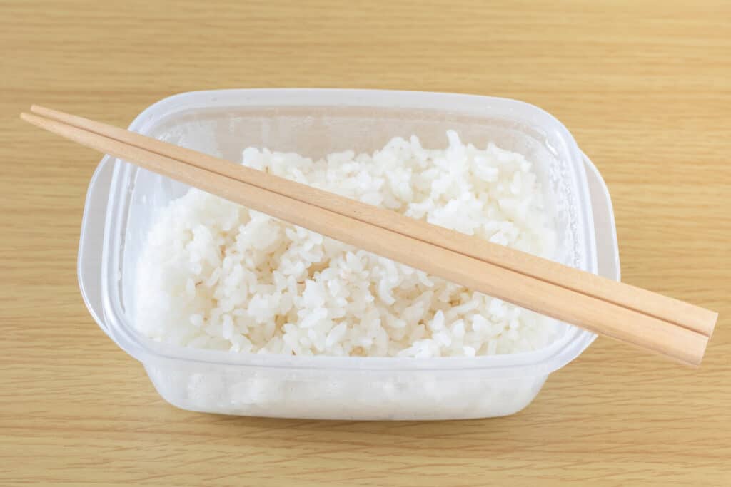 White rice in a Tupperware container with wooden chopsticks