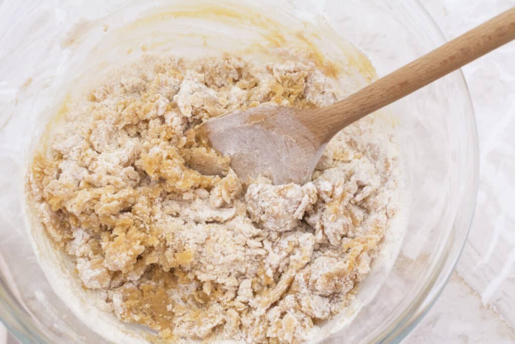 Stirring cookie dough together with a wooden spoon to make peanut butter cookies