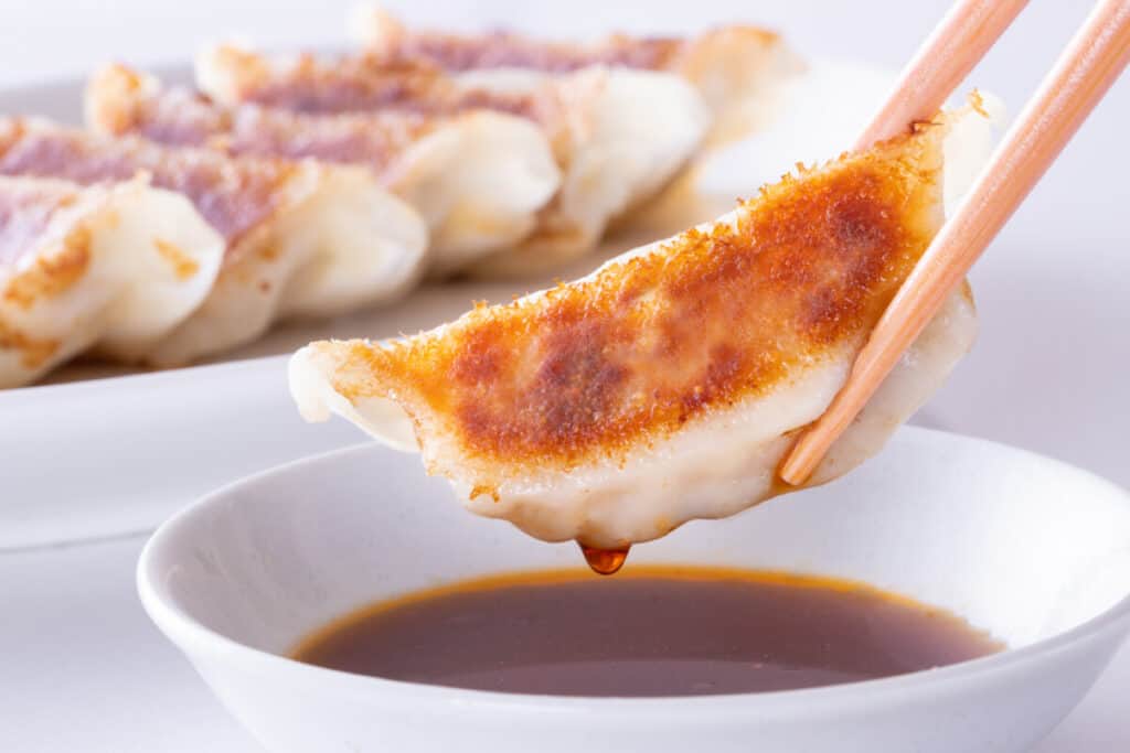 Fried dumpling being dipped in soy sauce with chop sticks