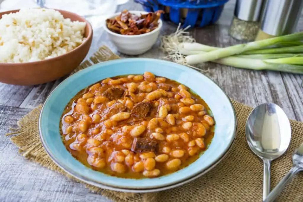 Blue bowl of baked beans with rice and green onions on burlap