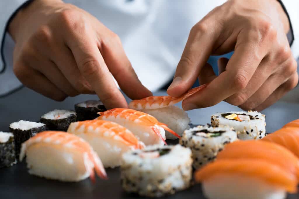 Chef making shrimp sushi and California rolls
