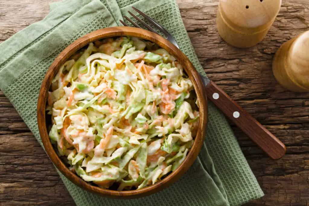 Coleslaw made of freshly shredded white cabbage and grated carrot with homemade mayonnaise-based salad dressing in wooden bowl