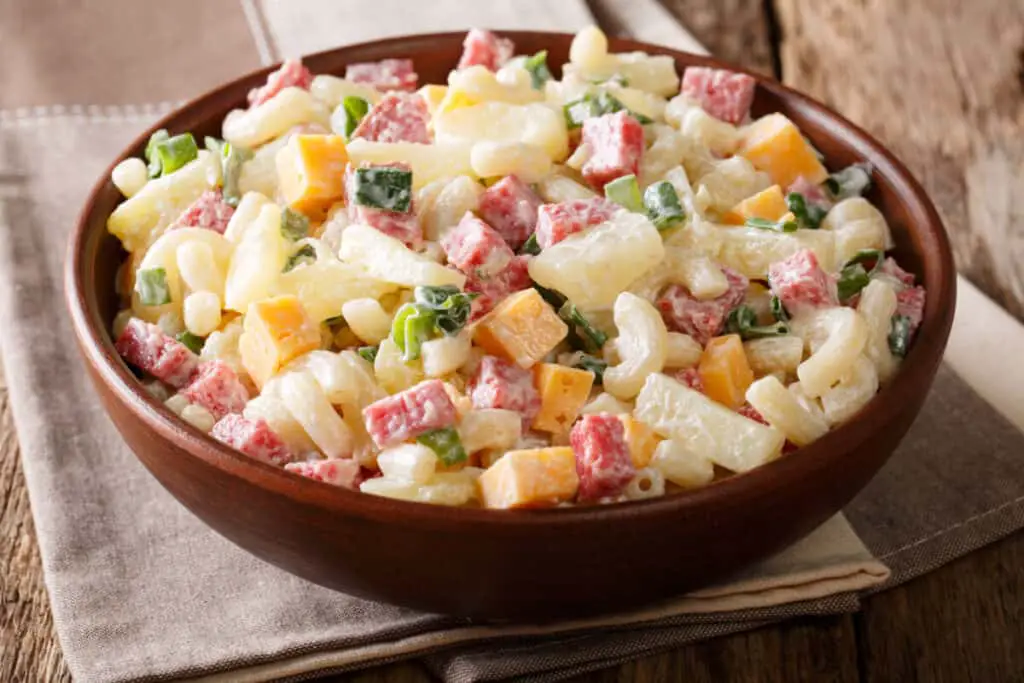 Pasta salad with ham, pineapple, onion, cheddar cheese, and in a wooden bowl on the table.