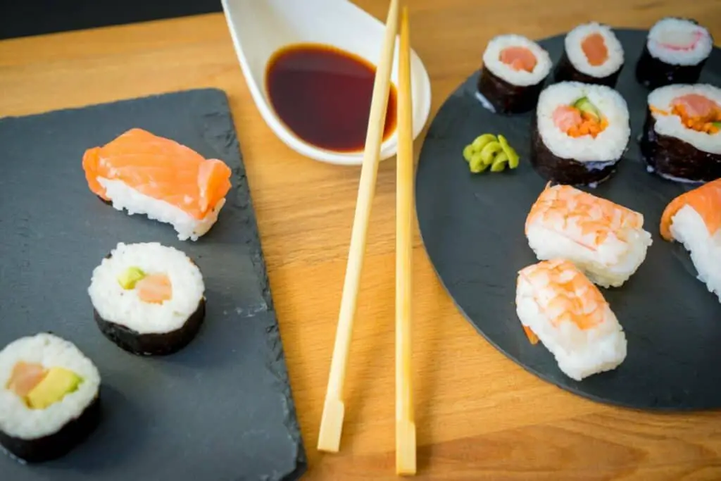 Shrimp sushi, salmon rolls, and California rolls on a black stone plate