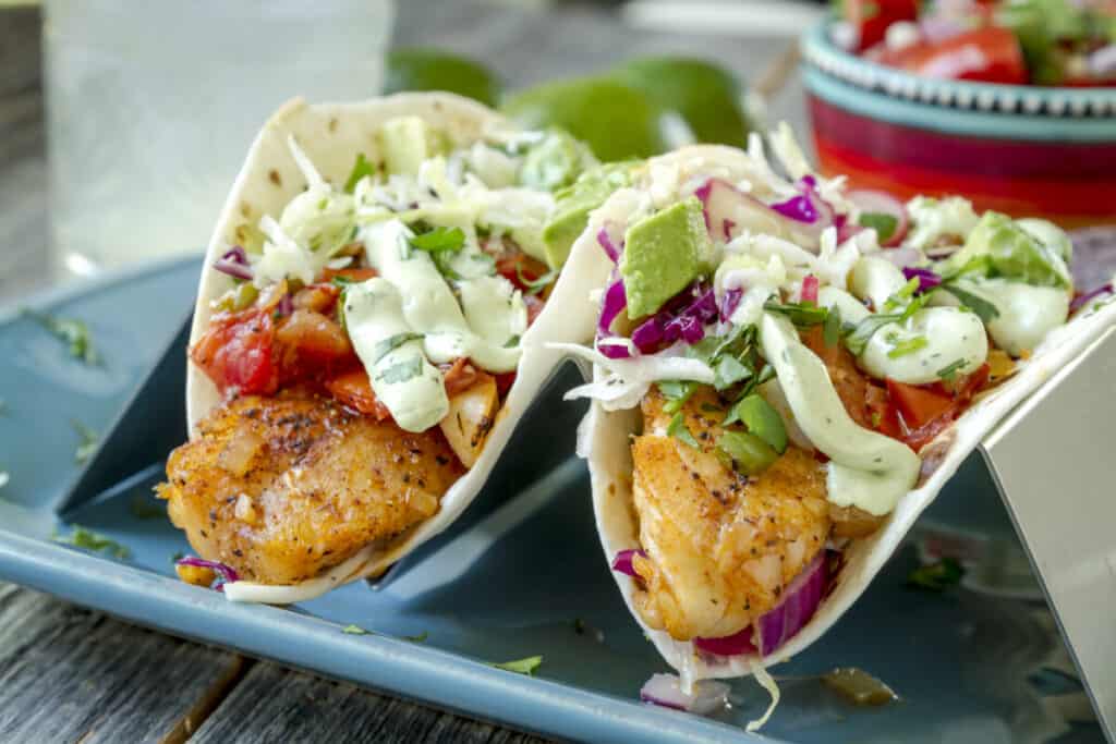 White fish tacos with fresh coleslaw, salsa, lime cream and avocado on blue plate