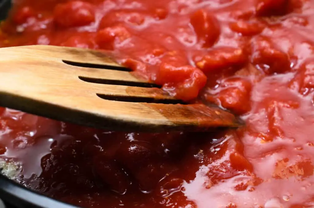 Bubbling hot tomato sauce for pasta, cooking in pan with wooden spatula.