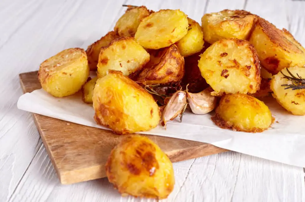 Roast potatoes seasoned with salt, garlic and rosemary on wood background.