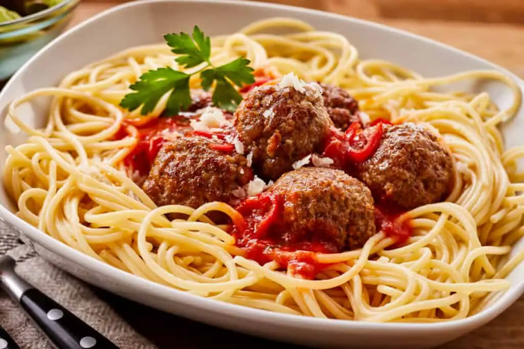 Homemade meatballs in tomato sauce on a bed of spaghetti noodles served in modern white bowl on table.