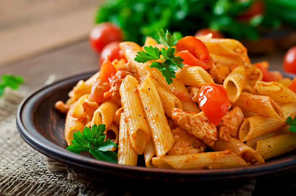 Penne pasta in tomato sauce with chicken and tomatoes on a wooden background.