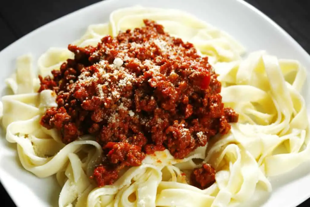 Spaghetti bolognese with parmesan cheese on a white plate on black table.