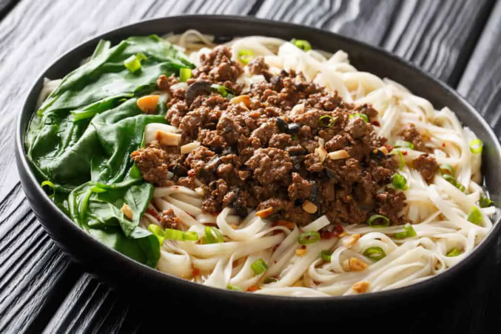 Traditional Chinese Sichuan Dan Dan Noodles with minced meat and greens in a plate on the table.