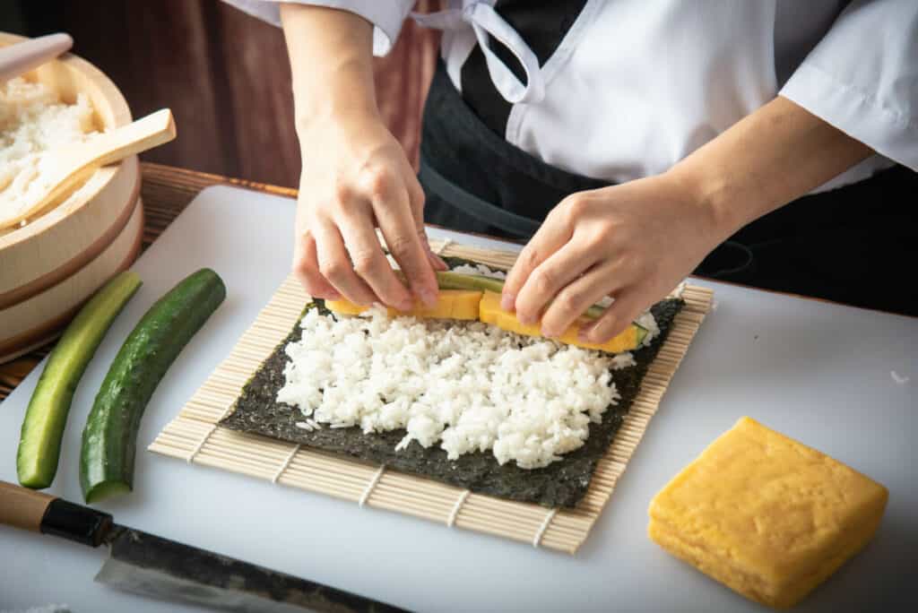 Sushi chef making roll sushi with cucumber and egg.