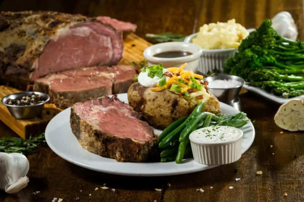 Prime rib meal served with green beans, baked potato, broccolini, mashed potatoes, and gravy.