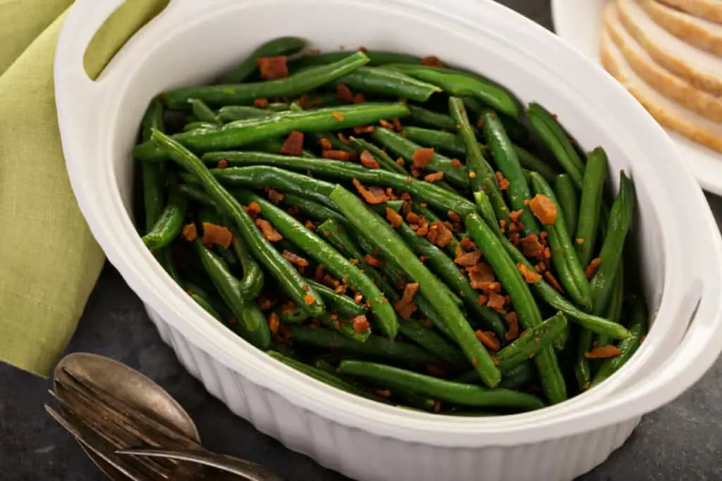 Green beans with crumbled bacon in a white casserole dish.