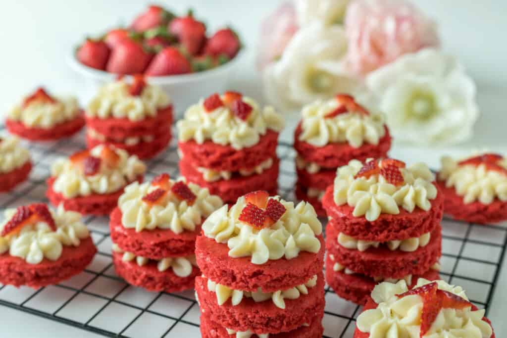 Miniature red velvet cakes with cream cheese frosting and fresh strawberry topping on a cooling rack.