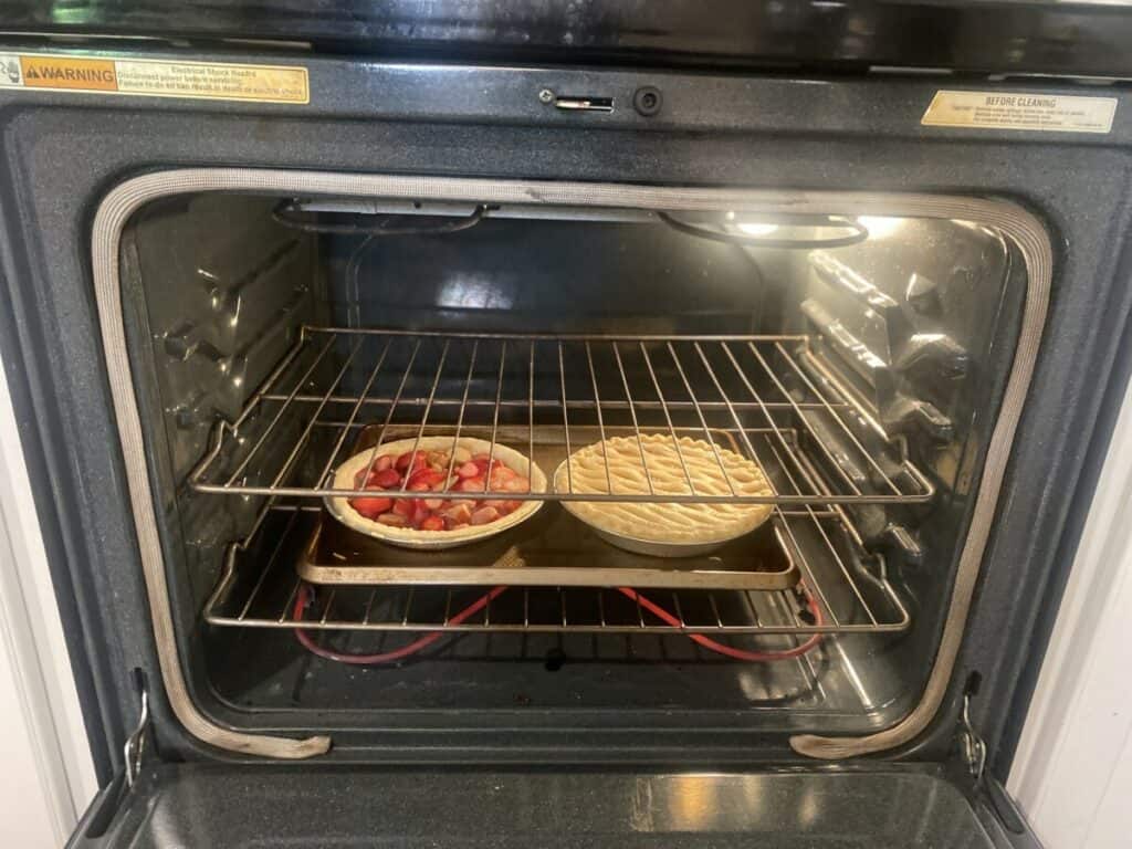 Strawberry and apple pies baking on the bottom rack of an oven.