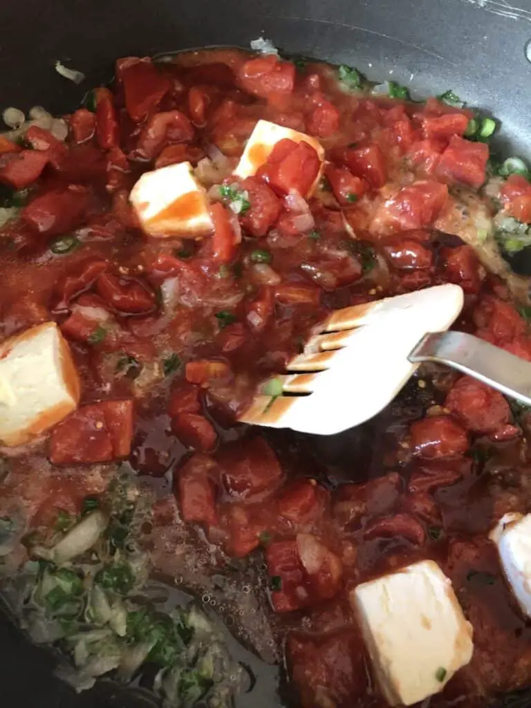 onions, tomatoes, and chicken being stirred in a pan